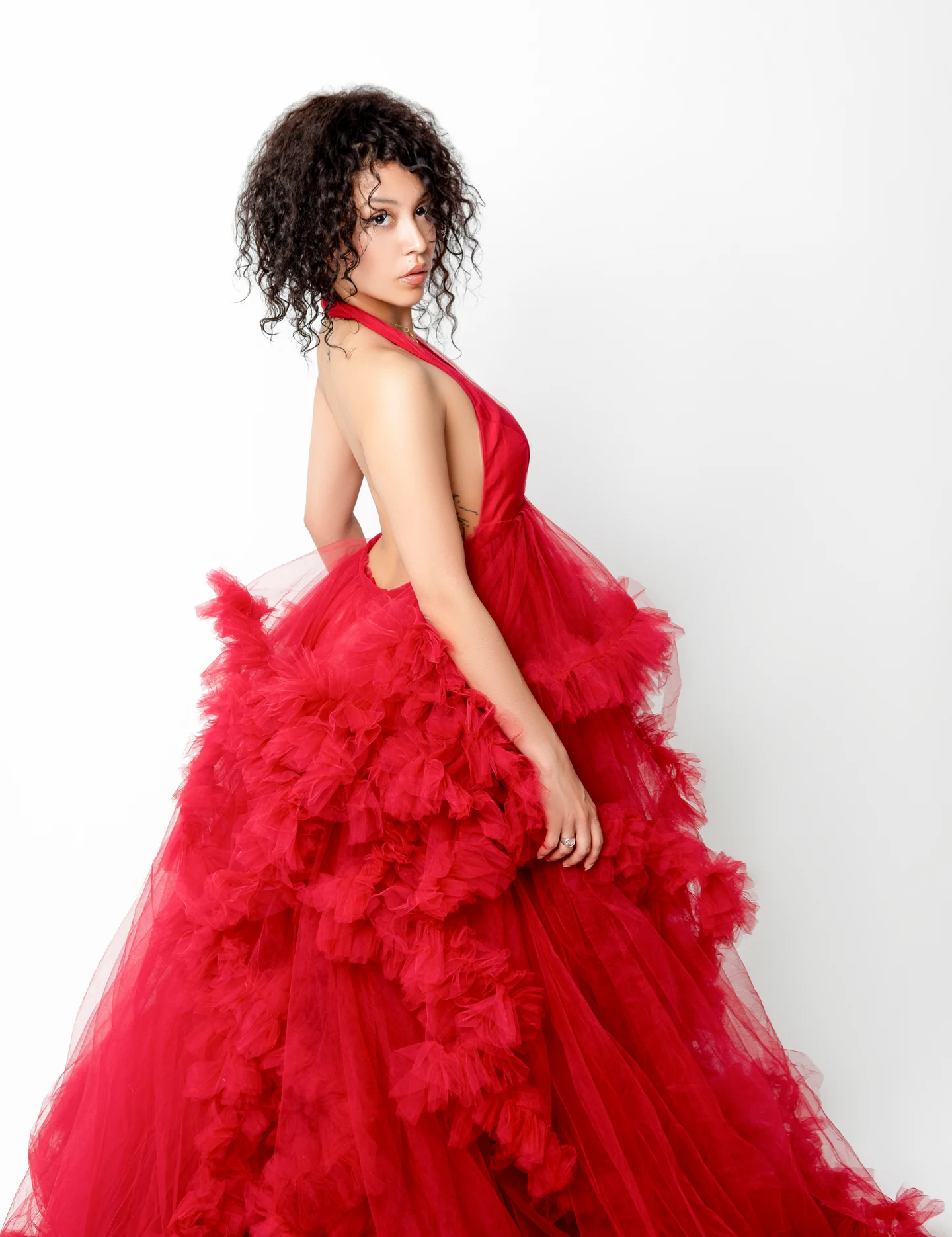 Une femme en robe rouge à volants, photographiée de trois quarts sur fond blanc.